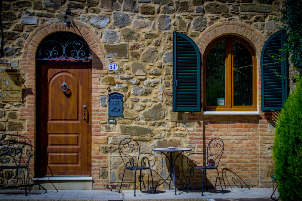 Wooden door, green shutters and a small table for two outside a Mediterranean guesthouse